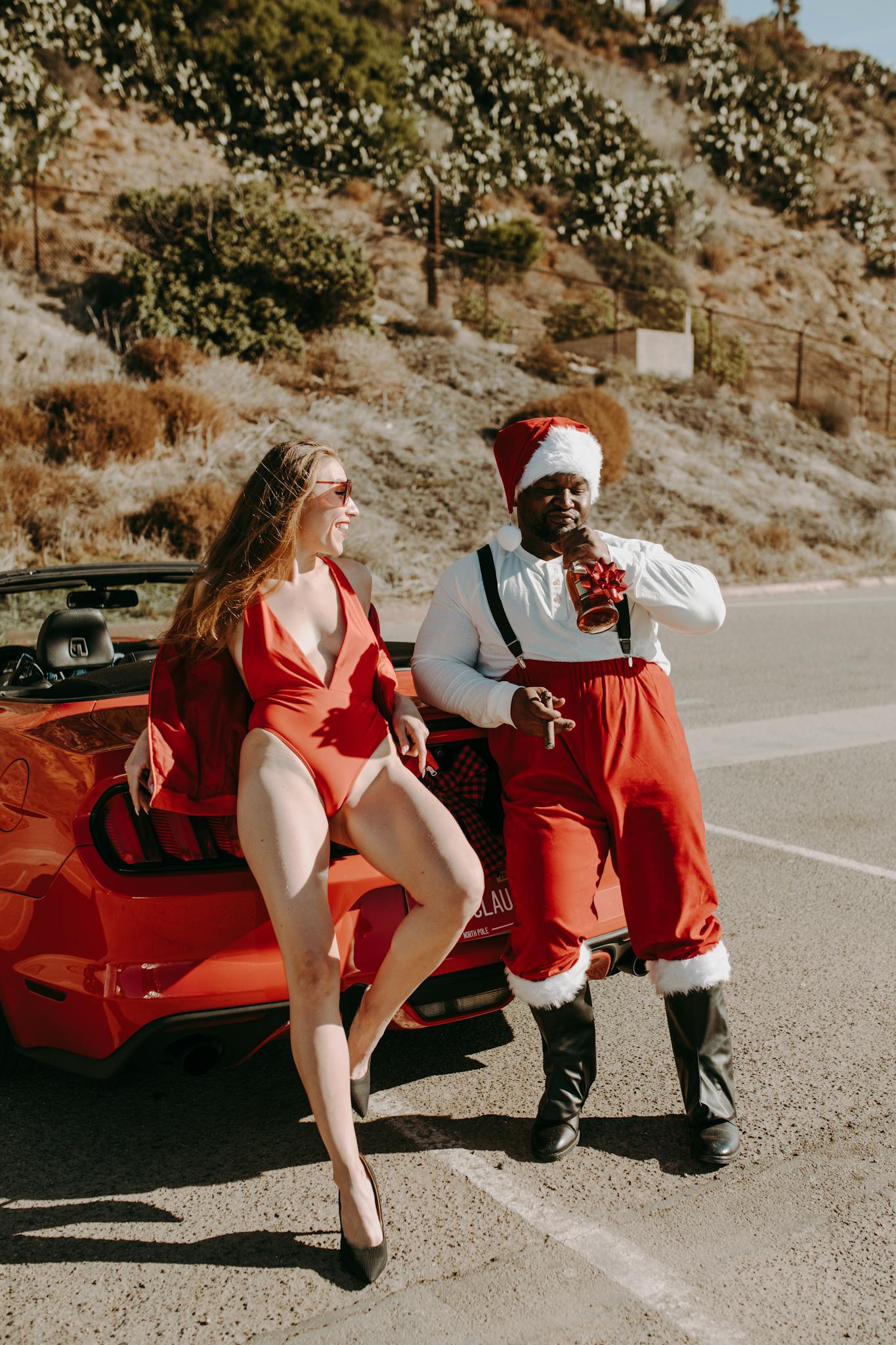 A fun outdoor Christmas scene with Santa and a friend in red attire next to a car.